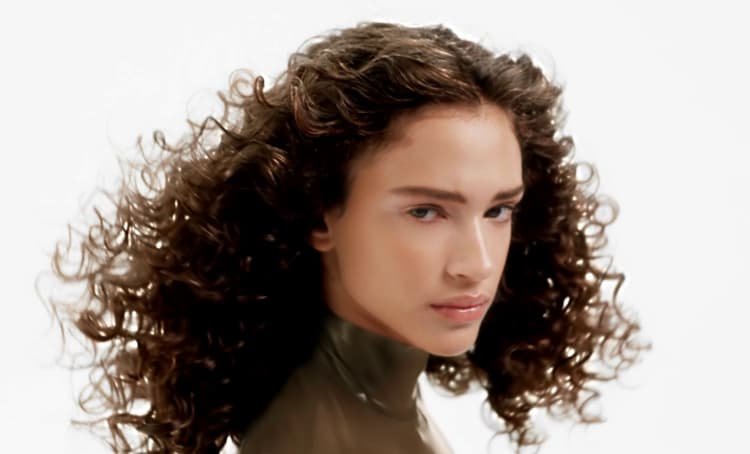 Woman posing and showing off her healthy, radiant, and well-defined curly hair with bounce, definition, and natural shine